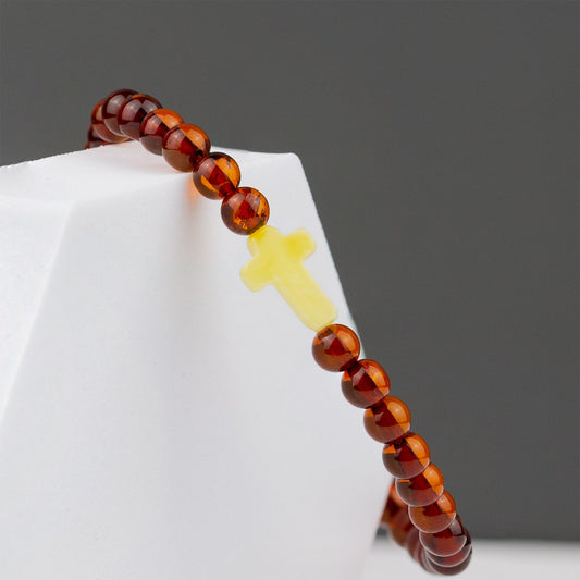 COGNAC CROSS, natūralaus gintaro apyrankė.
Poliruoto, šrato formos natūralaus gintaro detalės su kryželio formos akcentu. 
Detalių diametras:  5 – 5,5 mm. 
Vidinis Ilgis: 16 – 21 cm. 
Suverta ant elastingos, silikoninės gumos. 
Be užsegimo.