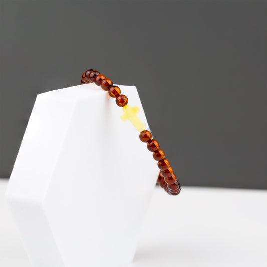COGNAC CROSS, natūralaus gintaro apyrankė.
Poliruoto, šrato formos natūralaus gintaro detalės su kryželio formos akcentu. 
Detalių diametras:  5 – 5,5 mm. 
Vidinis Ilgis: 16 – 21 cm. 
Suverta ant elastingos, silikoninės gumos. 
Be užsegimo.