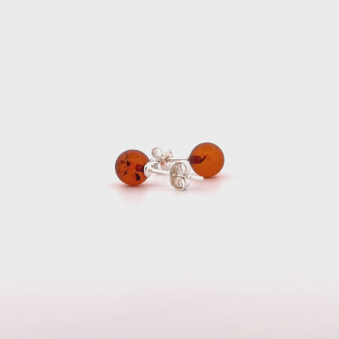 STUDS, Auskarai su natūraliu Baltijos gintaru.   Poliruotos, apvalios formos natūralaus gintaro detalės.  Gintaro diametras: 5 – 7 mm.  Išmatavimai: 5-7mm x 18 mm.  Sodraus konjako spalva.  Metalas: Ag 925 Sidabras. 